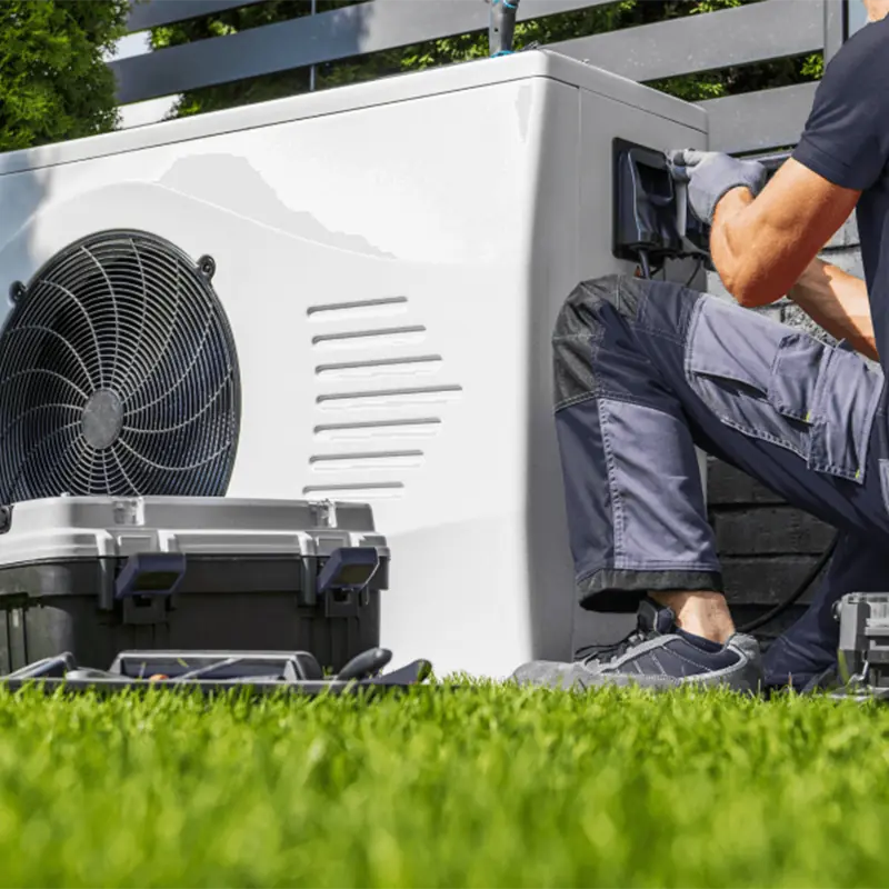 HVAC technician performing professional installation and electrical check on a modern residential heat pump outdoor unit